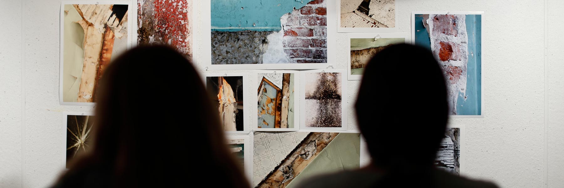 Two people look at photos on a wall.