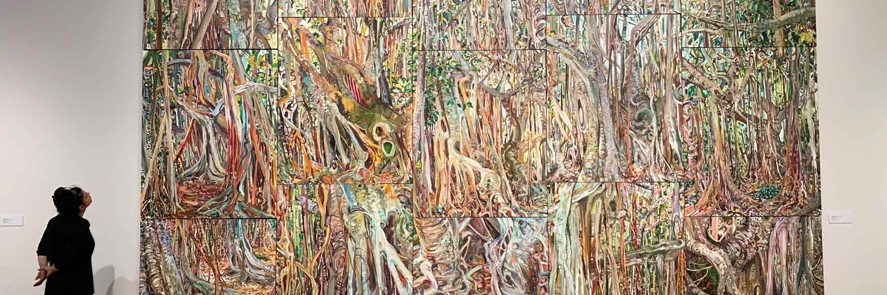 A person stares at a large colorful painting on the wall of a gallery.