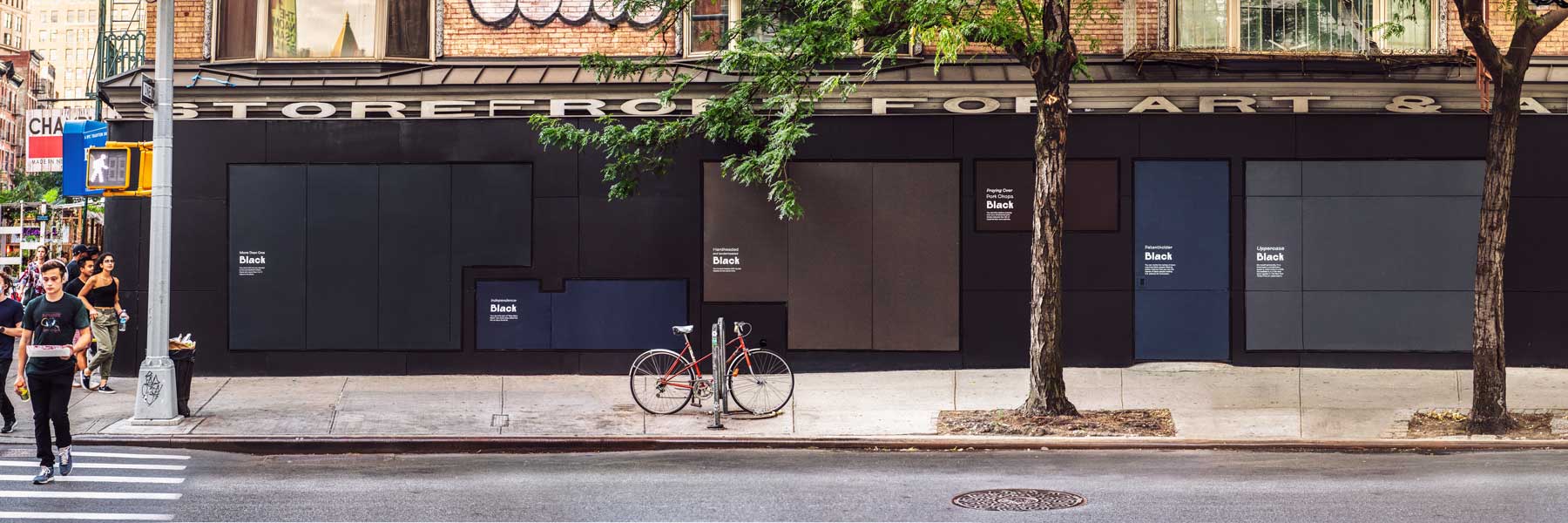A public artwork with different shades of black labeled on a large store front in a busy city.