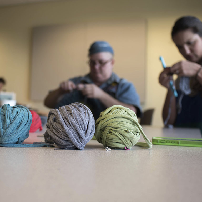 Balls of yarn and people crocheting with large hooks.