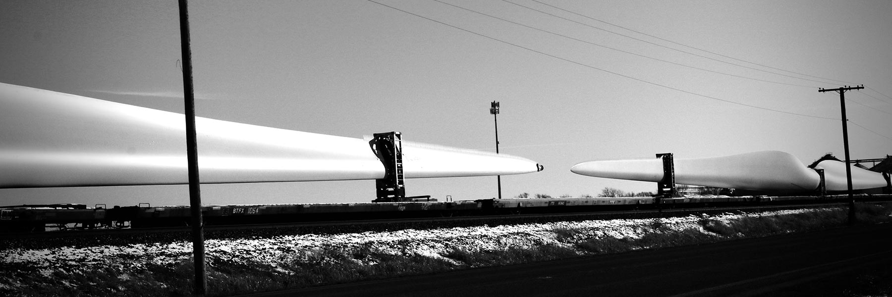 A black and white image of a field lined with a power line.