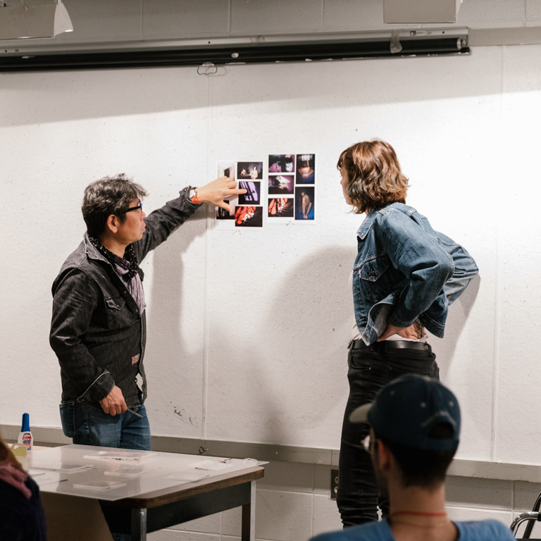 Two people look at photos on a wall.