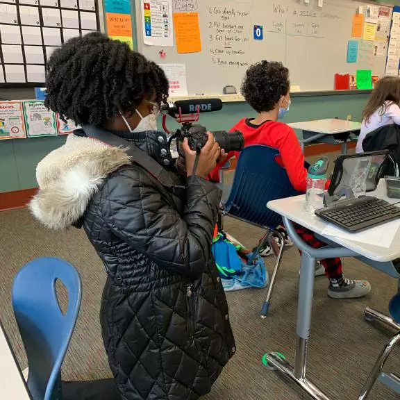 A student films a presentation in an elementary school classroom.