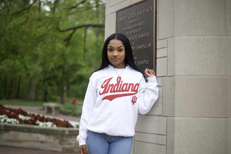 A person wearing a white Indiana University sweatshirt in front of a limestone archway. 