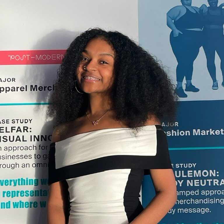 A person stands in front of a patterned background in a black and white dress, holding an award.