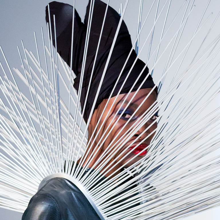 A person wearing a head wrap and a dress with white spikes fanning out from the shoulder